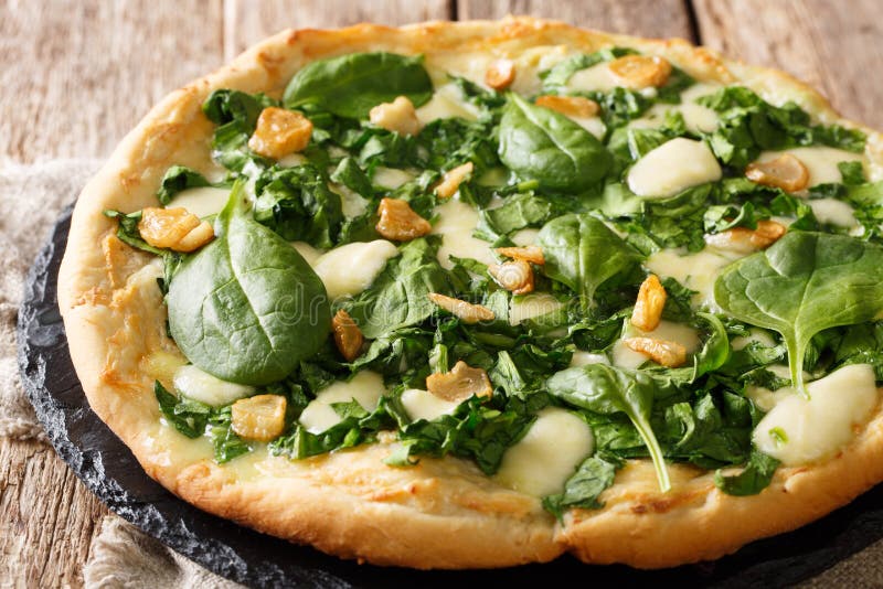 Pizza quente deliciosa com close-up fresco dos espinafres, do alho e do queijo em uma placa horizontal imagem de stock Pizza quente deliciosa com close-up fresco dos espinafres, do alho e do queijo em uma placa horizontal imagem de stock