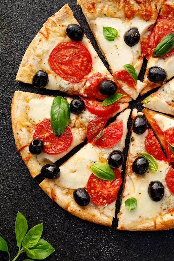 Pizza rebanadas con tomates, mozzarella, aceitunas negras y albahaca fresca sobre fondo negro, vista de arriba hacia abajo fotos de archivo libres de regalías Pizza rebanadas con tomates, mozzarella, aceitunas negras y albahaca fresca sobre fondo negro, vista de arriba hacia abajo fotos de archivo libres de regalías