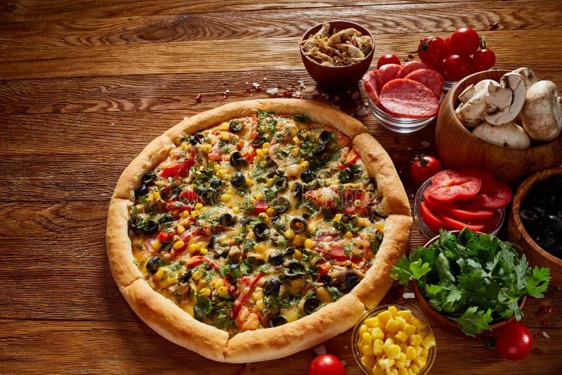 Pizza still life. Freshly baked pizza and its components arranged on wooden background.