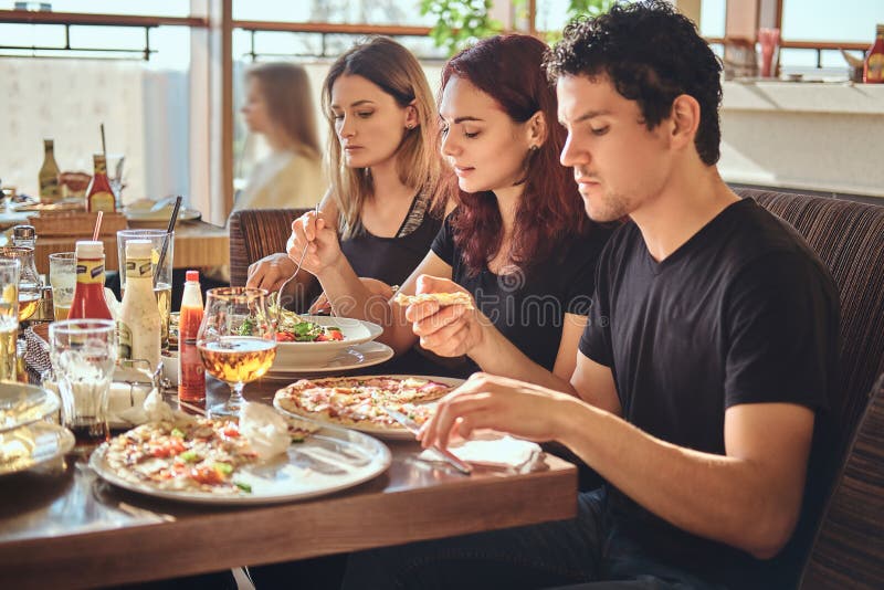 Pizzatijd Jonge vrienden die van pizza en salade in een openluchtkoffie genieten stock afbeelding Pizzatijd Jonge vrienden die van pizza en salade in een openluchtkoffie genieten stock afbeelding