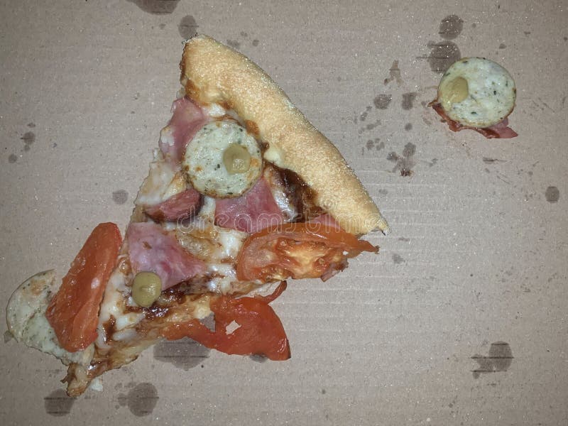 Pizze lasciate con carne e formaggio in una scatola. una fetta di pizza con salsiccia di prosciutto e pomodori fotografia stock libera da diritti