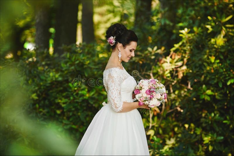 Piękna i elegancka młoda brunetki kobieta z modną fryzurą w eleganckiej ślubnej sukni z bukietem biel obrazy royalty free Piękna i elegancka młoda brunetki kobieta z modną fryzurą w eleganckiej ślubnej sukni z bukietem biel obrazy royalty free