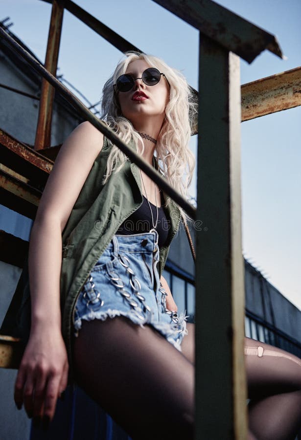 Piękna młoda grunge skały dziewczyna w skrótach, rozdzierającym pantyhose, koszula, kamizelce i czarnych szkłach, siedzi na drabi zdjęcia stock Piękna młoda grunge skały dziewczyna w skrótach, rozdzierającym pantyhose, koszula, kamizelce i czarnych szkłach, siedzi na drabi zdjęcia stock
