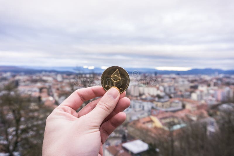 Pièce d'or d'Ethereum, prise Ethereum de main au-dessus de la ville photo libre de droits Pièce d'or d'Ethereum, prise Ethereum de main au-dessus de la ville photo libre de droits