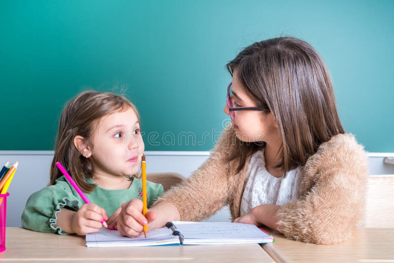 Più vecchi sguardi della sorella alla sua più giovane sorella come assorbe un taccuino immagine stock