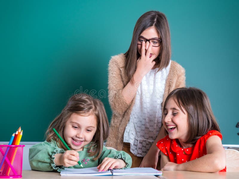 Più vecchi sguardi delle sorelle alla sua più giovane sorella come assorbe un taccuino fotografia stock
