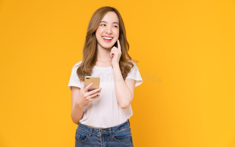 Piękna azjatka trzymająca smartfon i uśmiechająca się z pisaniem na żółtym tle obraz stock