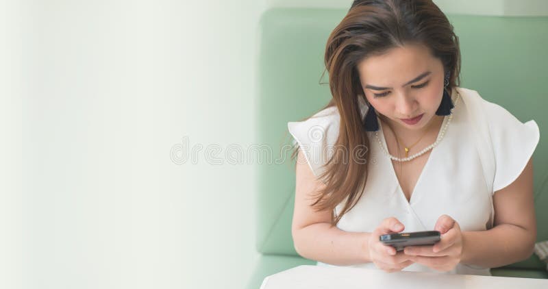 Piękna Azjatycka kobiety odzieży biała koszula na zielonej kanapie używać telefon komórkowy gadkę z przyjacielem i zamazanym tłem zdjęcia royalty free Piękna Azjatycka kobiety odzieży biała koszula na zielonej kanapie używać telefon komórkowy gadkę z przyjacielem i zamazanym tłem zdjęcia royalty free