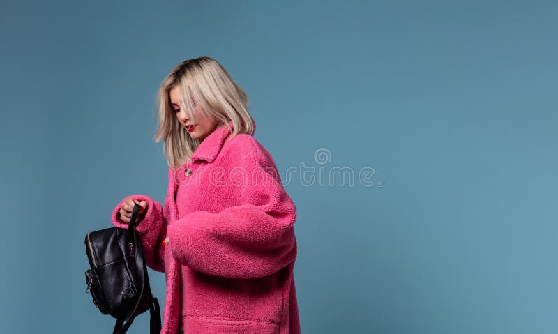Piękna blondynki dziewczyna jest ubranym menchie pokrywa trzymać czarnego plecaka w rękach fotografia stock Piękna blondynki dziewczyna jest ubranym menchie pokrywa trzymać czarnego plecaka w rękach fotografia stock