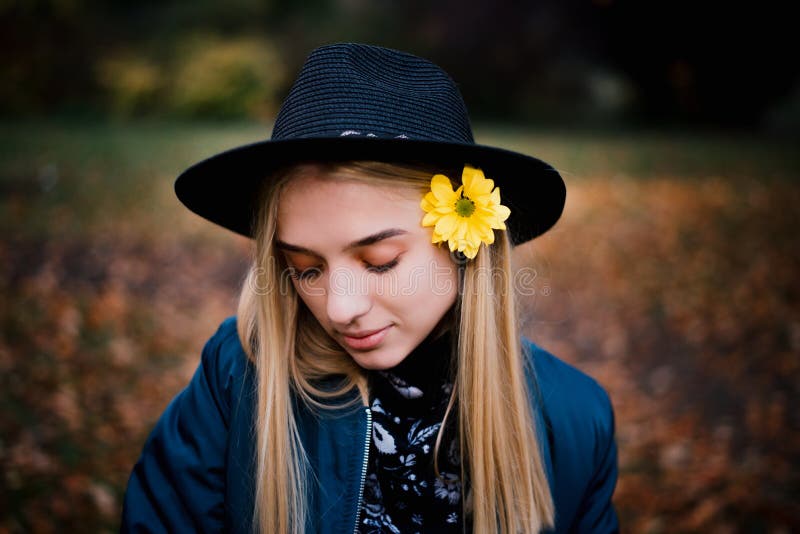 Piękna blondynki dziewczyna w kapeluszu w niebieskiej marynarce z żółtym kwiatem w jesień parku pełno żółci liście i obrazy stock Piękna blondynki dziewczyna w kapeluszu w niebieskiej marynarce z żółtym kwiatem w jesień parku pełno żółci liście i obrazy stock
