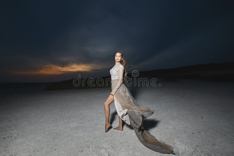 Piękna brunetka modela dziewczyna z długimi seksownymi nogami w modnej koronki smokingowy pozować przy dennym wybrzeżem przy zmie fotografia stock Piękna brunetka modela dziewczyna z długimi seksownymi nogami w modnej koronki smokingowy pozować przy dennym wybrzeżem przy zmie fotografia stock