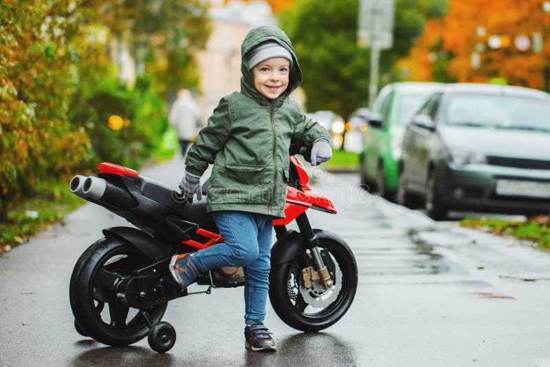 Piękna chłopiec pozuje przy jego dziecka ` s czerwieni motocyklem Pojęcie nauczań dzieci pojazdy mechaniczni od wczesnego zdjęcia stock Piękna chłopiec pozuje przy jego dziecka ` s czerwieni motocyklem Pojęcie nauczań dzieci pojazdy mechaniczni od wczesnego zdjęcia stock