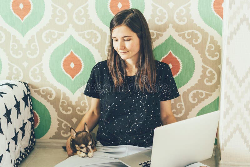 Piękna czuła dziewczyna siedzi na podłodze, trzymający pieszczotliwego Chuahuahua domu psa i laptop Freelance w sposobie obraz stock Piękna czuła dziewczyna siedzi na podłodze, trzymający pieszczotliwego Chuahuahua domu psa i laptop Freelance w sposobie obraz stock
