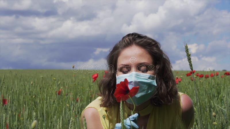 Piękna dziewczyna w masce ochronnej i rękawiczkach na polu pszenicy zielone z czerwonym makiem wącha kwiat. epidemia koronawirusa zbiory