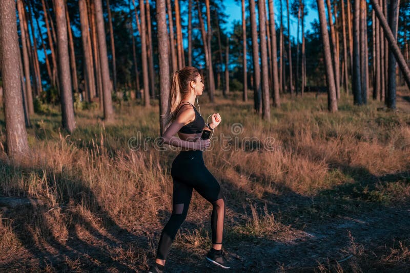 Piękna dziewczyna w sportswear bieg na bieg Kobieta słucha muzyka w lecie w lesie Z hełmofonami fotografia royalty free Piękna dziewczyna w sportswear bieg na bieg Kobieta słucha muzyka w lecie w lesie Z hełmofonami fotografia royalty free