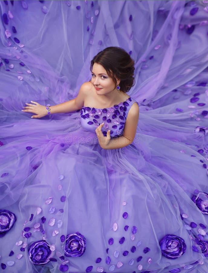 Beautiful young brunette in luxury, purple, long dress in the petals of a flower. Outfit-exclusive handmade. Photo Fairy. Queen with a mysterious smile. Fashionable toning. Creative computer colors. Beautiful young brunette in luxury, purple, long dress in the petals of a flower. Outfit-exclusive handmade. Photo Fairy. Queen with a mysterious smile. Fashionable toning. Creative computer colors.