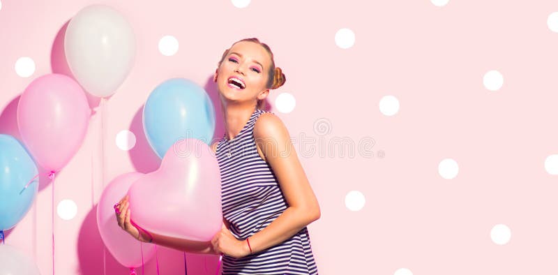 Beauty girl with colorful air balloons laughing over pink background. Beautiful Happy Young woman on birthday holiday party. Joyful model having fun, playing and celebrating with pastel color balloon. Beauty girl with colorful air balloons laughing over pink background. Beautiful Happy Young woman on birthday holiday party. Joyful model having fun, playing and celebrating with pastel color balloon