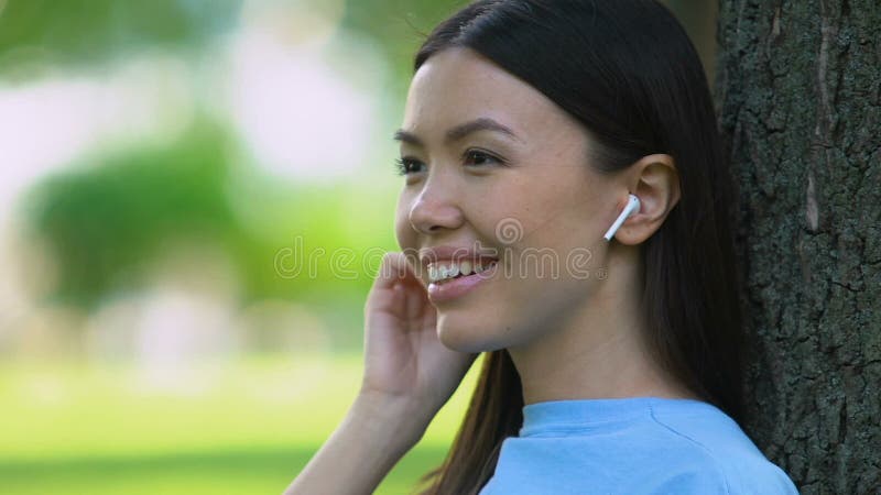 Piękna kobieta słuchająca muzyki przez bezprzewodowe słuchawki, relaksująca się w parku