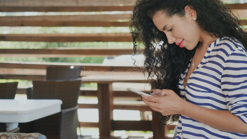 Piękna kędzierzawa brunetka używać smartphone na lato tarasie