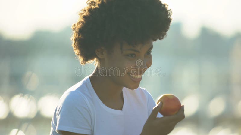 Piękna kędzierzawa z włosami kobieta je świeżego jabłka outdoors, zdrowy łasowanie, dieta