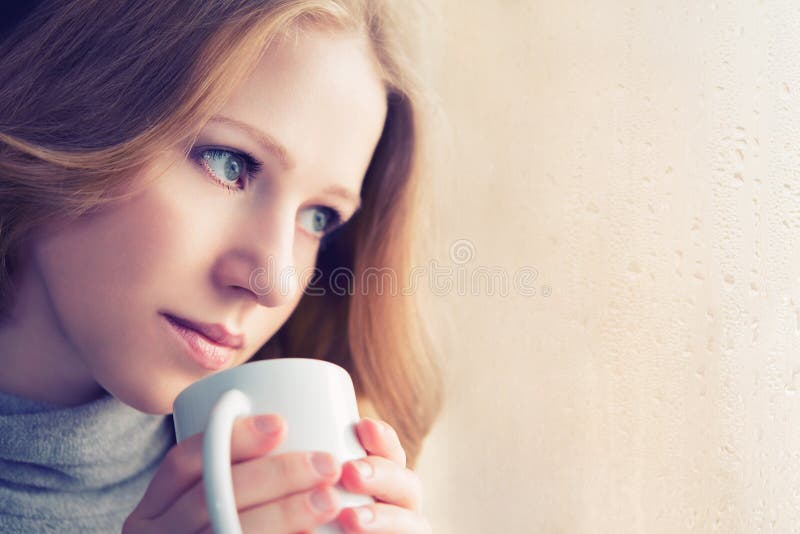 Piękna marzycielska dziewczyna z filiżanką gorąca kawa przy okno