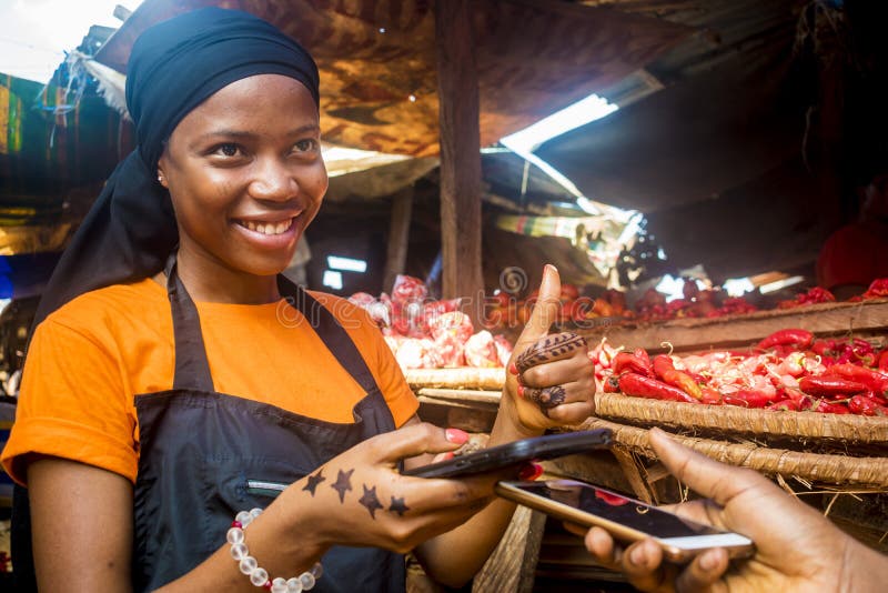 Piękna, młoda czarna kobieta sprzedająca pomidory na lokalnym rynku afrykańskim otrzymująca płatność za pośrednictwem przekazu te
