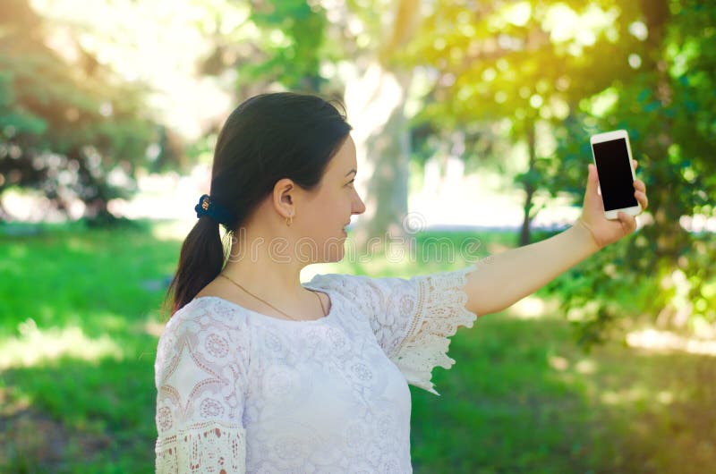 Piękna młoda Europejska dziewczyny brunetka bierze obrazek ona i robi selfie w miasto parku ludzie, styl życia, chodzi wewnątrz obraz royalty free Piękna młoda Europejska dziewczyny brunetka bierze obrazek ona i robi selfie w miasto parku ludzie, styl życia, chodzi wewnątrz obraz royalty free