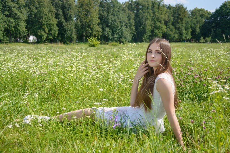 Piękna młoda kobieta siedzi w kwiecistej łące w białej sukience