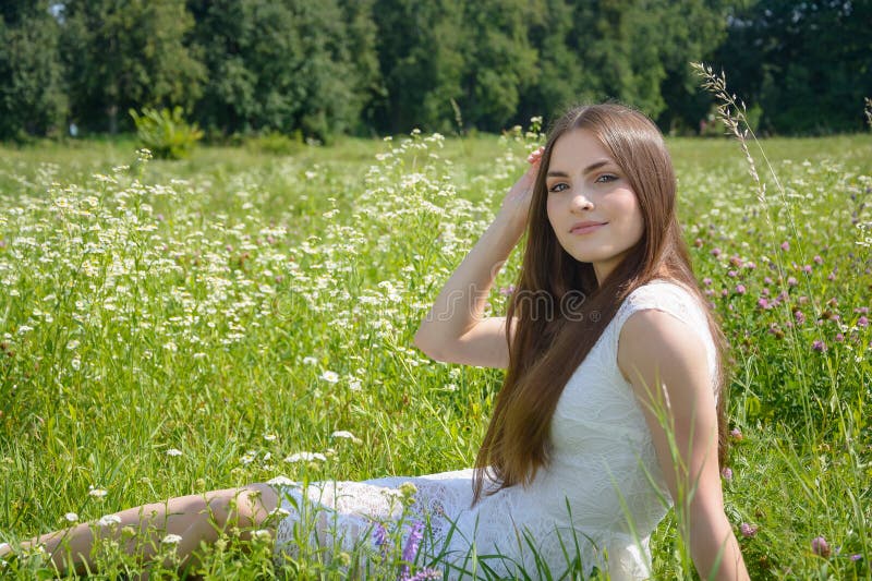 Piękna młoda kobieta siedzi w kwiecistej łące w białej sukience