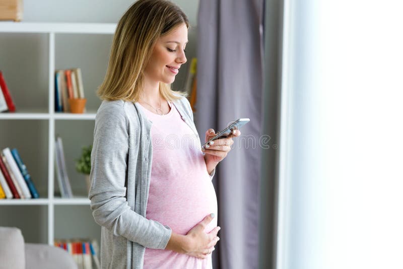 Piękna młoda kobieta w ciąży texting z jej smartphone w domu zdjęcie royalty free Piękna młoda kobieta w ciąży texting z jej smartphone w domu zdjęcie royalty free
