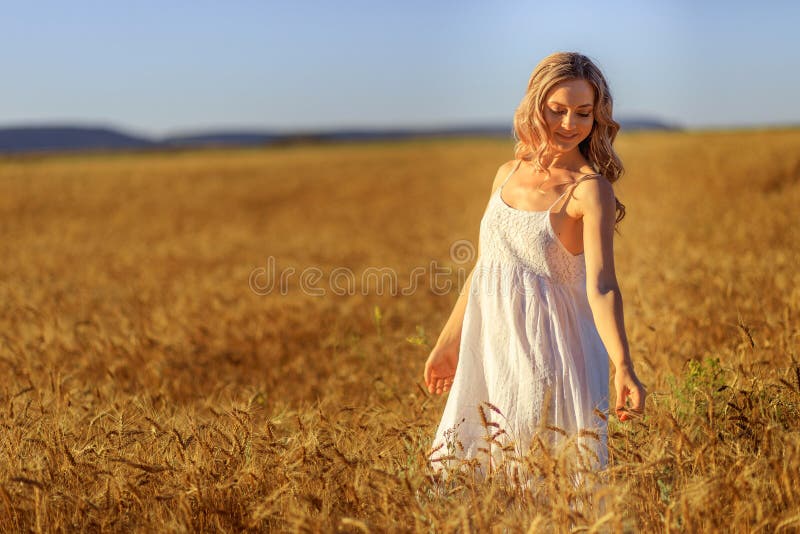 Piękna młoda kobieta w pszenicznym polu przy zmierzchem plenerowym
