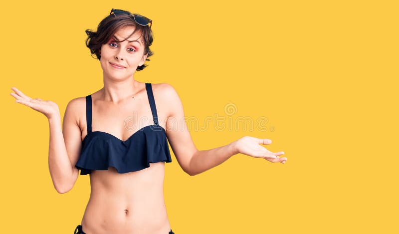 Piękna młoda kobieta z krótką fryzurą w bikini, bez kłótni i zmieszanym wyrazem z podniesionymi rękami i rękami fotografia royalty free
