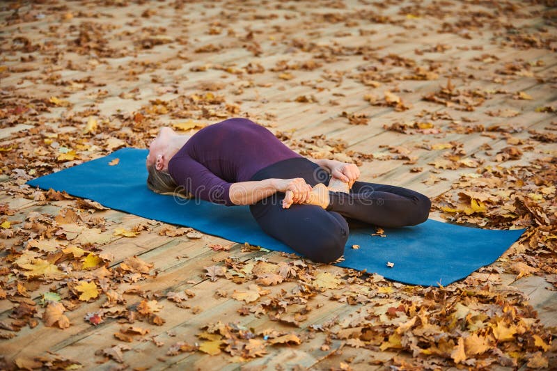 Piękna młoda kobieta ćwiczy joga asana Matsyasana - Rybia poza na drewnianym pokładzie w jesień parku fotografia stock Piękna młoda kobieta ćwiczy joga asana Matsyasana - Rybia poza na drewnianym pokładzie w jesień parku fotografia stock