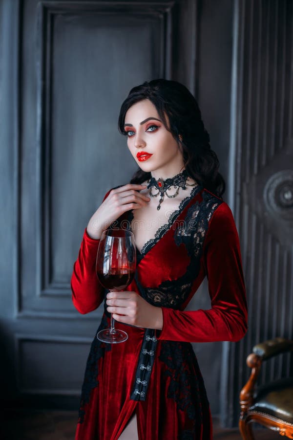 Beautiful young sexy woman vampire in medieval dark castle. Red gothic evening dress. Black wavy hair. Backdrop vintage room. A girl holding a glass of bloody wine in her hands. Image queen of night. Beautiful young sexy woman vampire in medieval dark castle. Red gothic evening dress. Black wavy hair. Backdrop vintage room. A girl holding a glass of bloody wine in her hands. Image queen of night.
