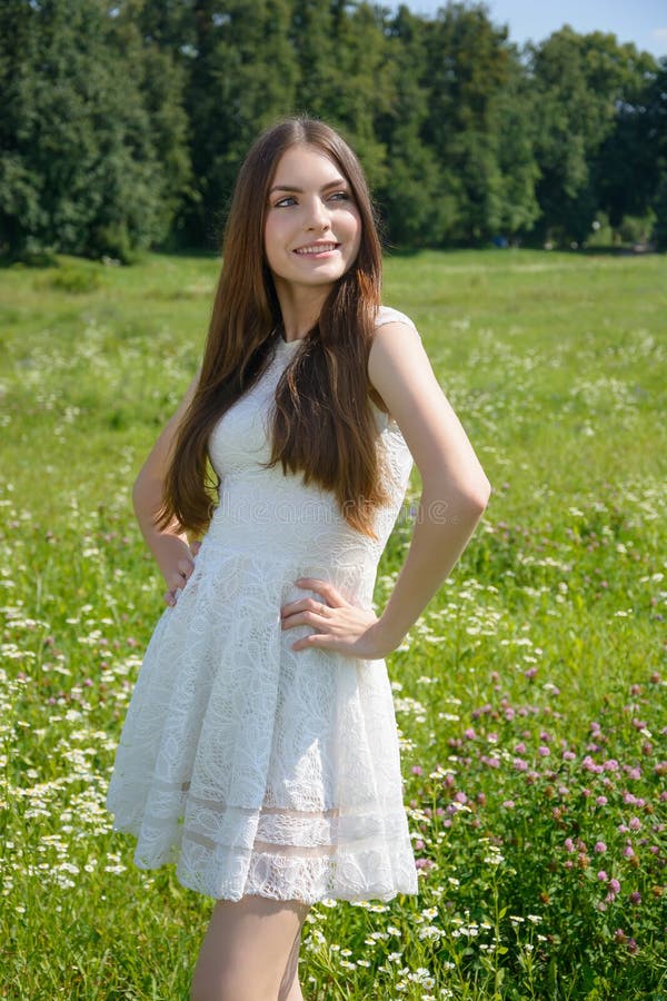 Piękna młoda uśmiechnięta kobieta w kwiecistej łące w białej sukience