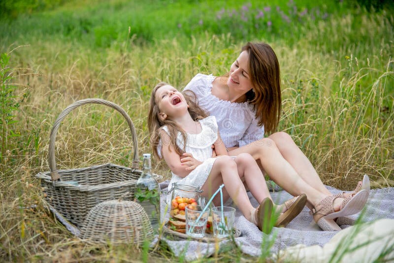 Piękna potomstwo matka i jej mała córka w bielu ubieramy mieć zabawę w pinkinie na letnim dniu Siedzą na dywaniku i fotografia royalty free Piękna potomstwo matka i jej mała córka w bielu ubieramy mieć zabawę w pinkinie na letnim dniu Siedzą na dywaniku i fotografia royalty free