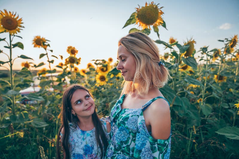 Piękna, szczęśliwa, młoda blondynka mama i jej brunetka córka uśmiechają się i patrzą na siebie, stojąc pośród obraz stock Piękna, szczęśliwa, młoda blondynka mama i jej brunetka córka uśmiechają się i patrzą na siebie, stojąc pośród obraz stock