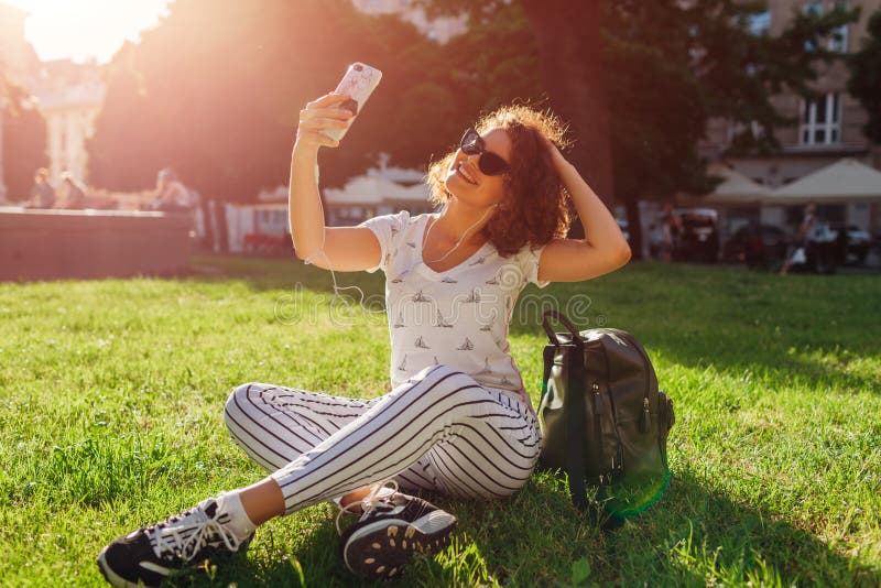 Piękna szkoły wyższa dziewczyna bierze selfie i słuchanie muzyka w kampusu parku zdjęcie stock Piękna szkoły wyższa dziewczyna bierze selfie i słuchanie muzyka w kampusu parku zdjęcie stock