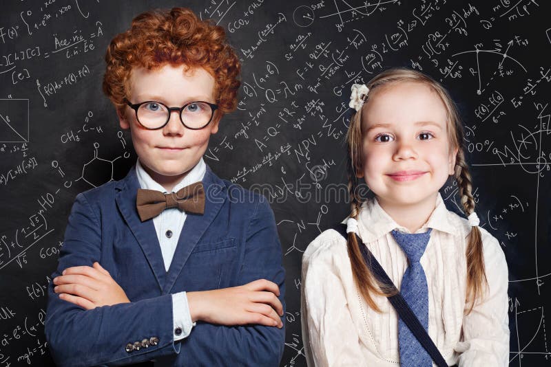 PiÄ™kne dzieciaki. Uczennica szkoÅ‚y dla maÅ‚ych dzieci na czarnej tablicy z formuÅ‚ami matematycznymi i naukowymi zdjęcie stock