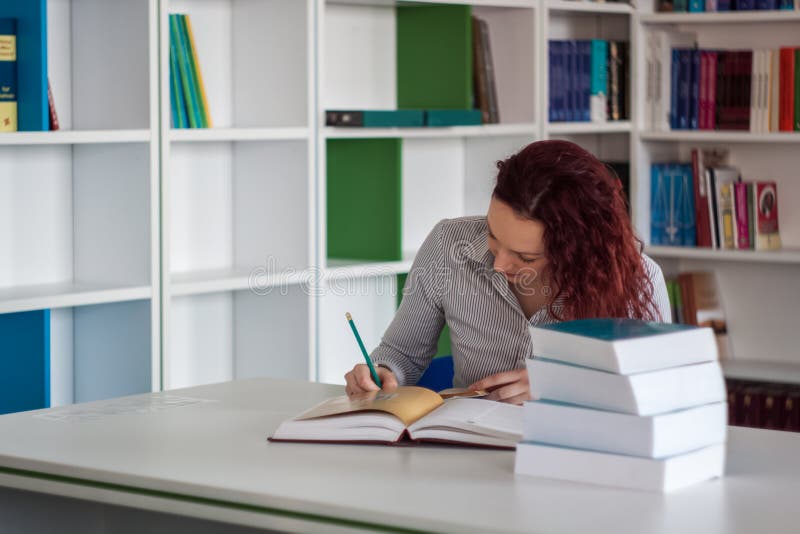Piękne rudzielec dziewczyny writing notatki w notatniku z stosem obraz stock Piękne rudzielec dziewczyny writing notatki w notatniku z stosem obraz stock