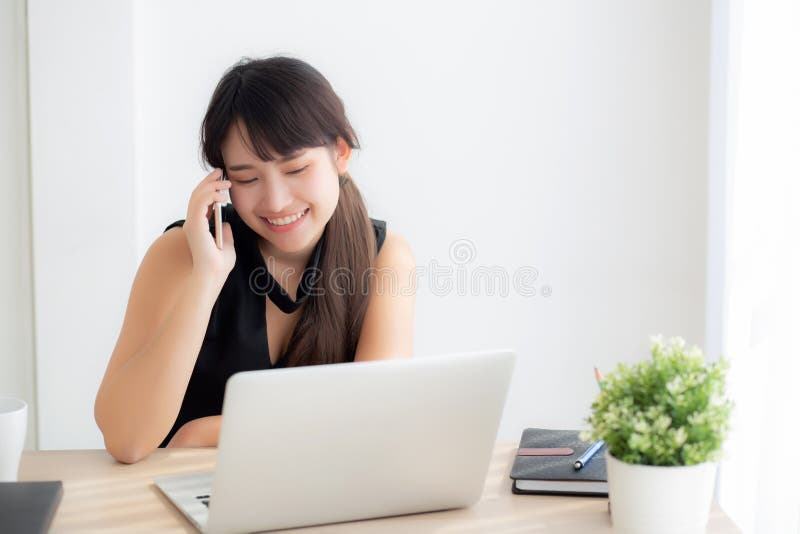 Pięknej młodej freelance azjatykciej kobiety uśmiechnięty działanie na laptopie i opowiadać mobilnego mądrze telefon przy biurka zdjęcia royalty free Pięknej młodej freelance azjatykciej kobiety uśmiechnięty działanie na laptopie i opowiadać mobilnego mądrze telefon przy biurka zdjęcia royalty free
