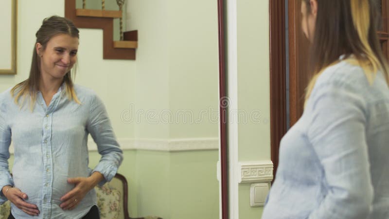 Piękni kobieta w ciąży stojaki przed lustrem