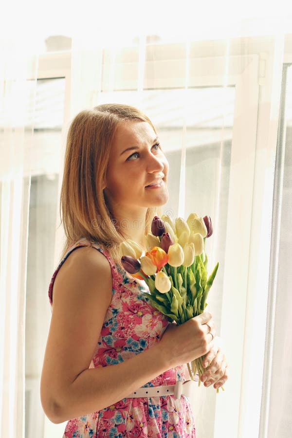 Piękni uśmiechnięci kobieta tulipany stoją blisko dużego okno obraz stock Piękni uśmiechnięci kobieta tulipany stoją blisko dużego okno obraz stock