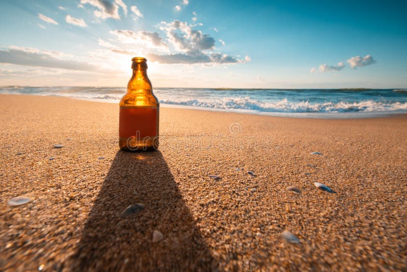 Piękny denny wschód słońca i piwna butelka na plażowym piasku fotografia stock