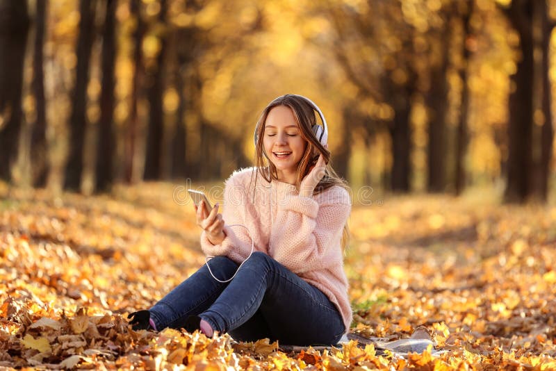 Young beautiful girl sitting with headphones and smartphone in autumn park. Young beautiful girl sitting with headphones and smartphone in autumn park