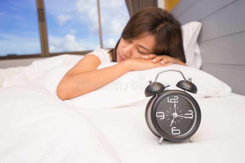 Piękny młodej kobiety dosypianie i ono uśmiecha się podczas gdy kłamający w łóżku swobodnie i blissfully na tle budzik obrazy stock Piękny młodej kobiety dosypianie i ono uśmiecha się podczas gdy kłamający w łóżku swobodnie i blissfully na tle budzik obrazy stock