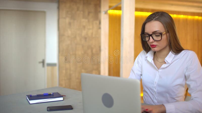 Piękny młody bizneswoman jest ubranym szkła i działanie przy nocą używać nowożytnego komputerowego ekran sensorowego, ufna kobiet