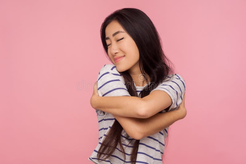 I`m beautiful. Portrait of attractive narcissistic brunette girl in t-shirt embracing herself and smiling with pleasure, satisfied with appearance. indoor studio shot isolated on pink background. I`m beautiful. Portrait of attractive narcissistic brunette girl in t-shirt embracing herself and smiling with pleasure, satisfied with appearance. indoor studio shot isolated on pink background