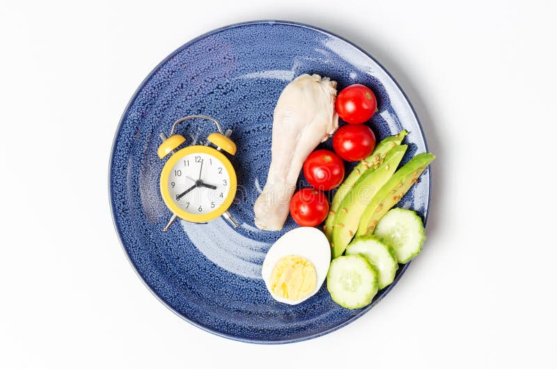 Plate with vegetables and alarm clock on white background, intermittent fasting concept. Plate with vegetables and alarm clock on white background, intermittent fasting concept