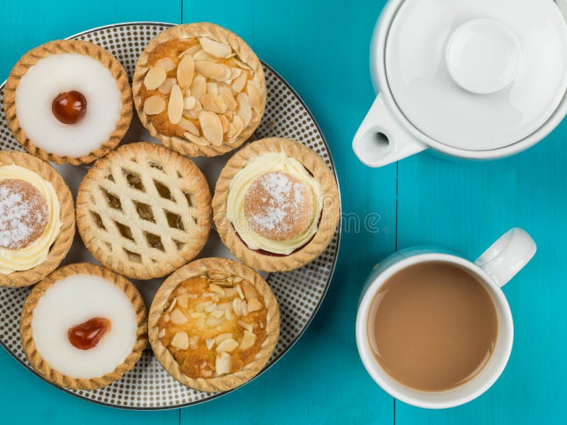 Plate of Assorted Individual Cakes or Tarts With a Pot of Tea Against a Blue Background. Plate of Assorted Individual Cakes or Tarts With a Pot of Tea Against a Blue Background